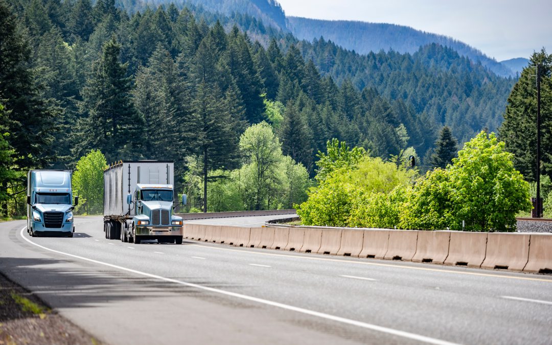 Two semi-trucks on a highway surrounded by lush green trees, representing opportunities for truck drivers in spring.