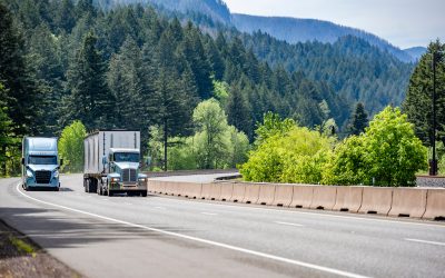 Two commercial trucks driving on a highway surrounded by lush greenery and mountains, illustrating the open road and opportunities for truck drivers.
