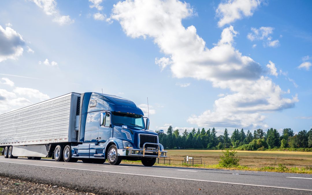 Blue semi-truck on highway with scenic landscape, representing commercial driving safety and regulations in the trucking industry.